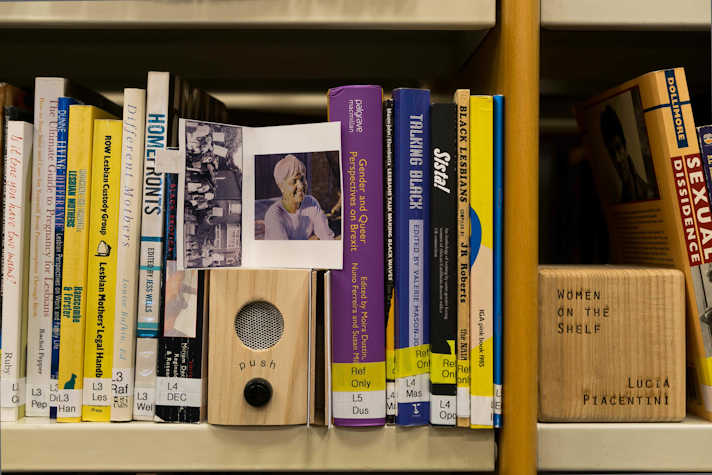 Close up view of some books on a shelf with a small speaker inserted between them and a photo resting on top of the speaker
