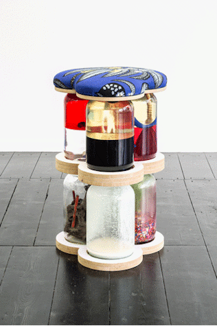 The image shows a sculpture of 6 large glass jars stacked and filled with materials