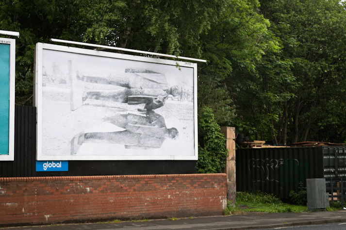 a billboard displays an intricate pencil drawing of a toppled statue