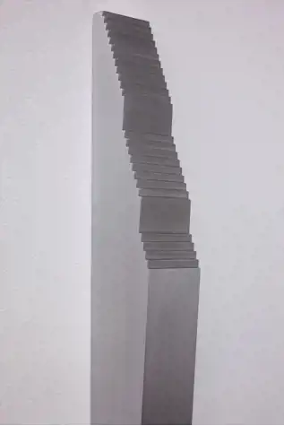 close up of an aluminium abstract sculpture mounted on a white wall that resembles a flight of stairs leading to a ramp