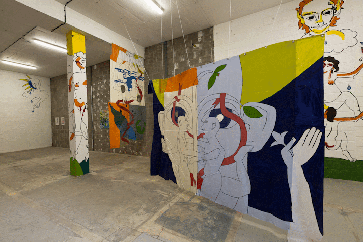 Playful and surreal line drawings of figures with blocks of colour cover a wall, column and fabric hanging in an industrial space