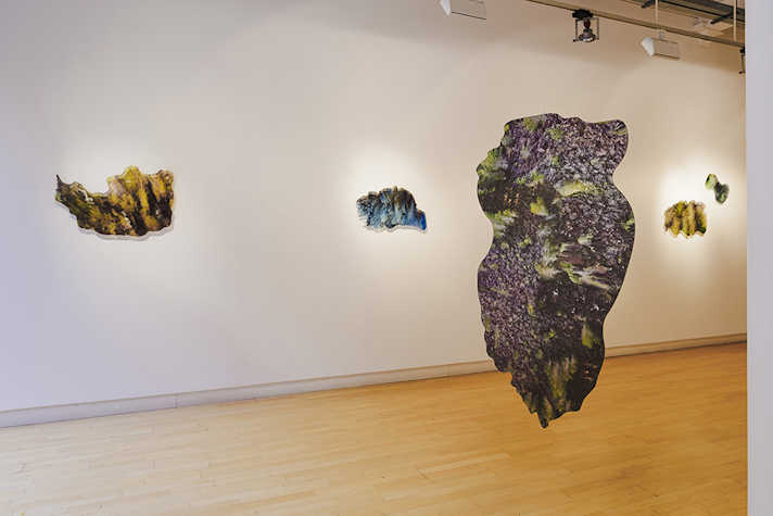 A patterned, abstract shape hangs from the ceiling in the foreground. Behind on a wall, more shapes are displayed with lights shining from behind them.
