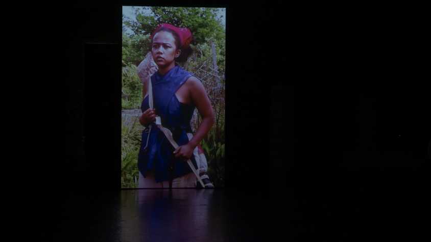 completely dark scene apart from an illuminated image of a person stood in front of trees.