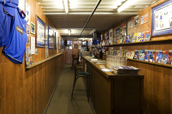 narrow interior of a wood panelled Glasgow Rangers themed pub like location with a long table/bar with glasses atop