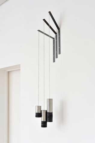 three metal cylinders with the bottoms covered in a black rusty coating. they hang from chains attached to a fixture on the wall.