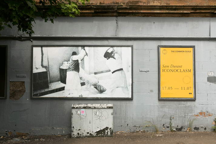 a billboard displays an intricate pencil drawing of two figures toppling a statue