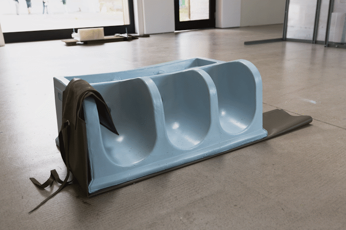 abstract pale blue sculpture with khaki leather sits on a gallery floor