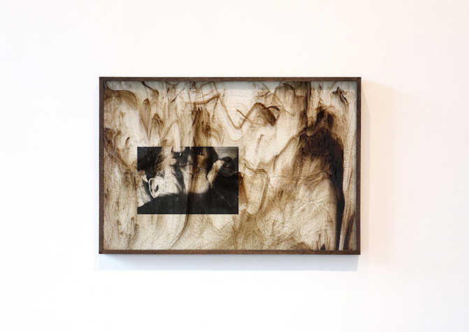 A framed artwork featuring oil-like marks and a faded black and white photograph.