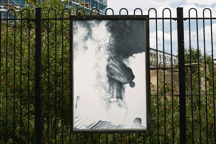 a billboard displays an intricate pencil drawing of a statue in flames and toppling