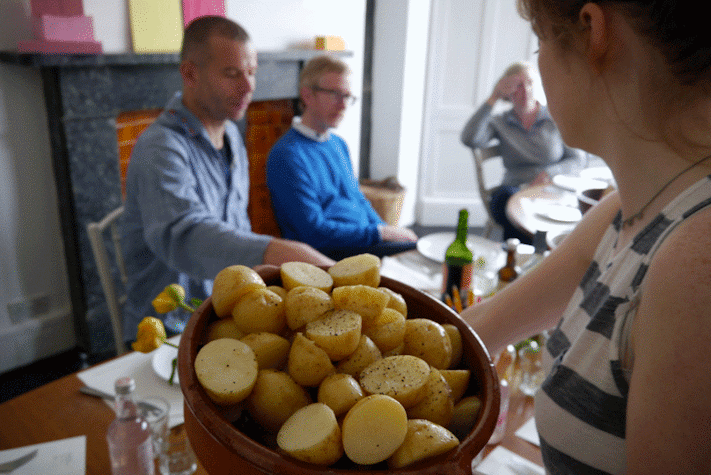 woman holding a bowl of boiled potatoes with guests dining in background
