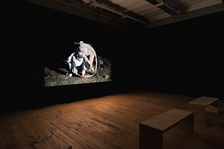 Film is projected onto a screen in a dark room. There are wooden benches facing the screen.