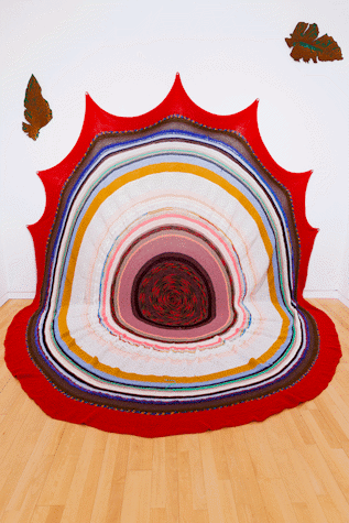 A large circular piece of fabric is displayed against a wall and floor, it features many smaller circles in different colours.