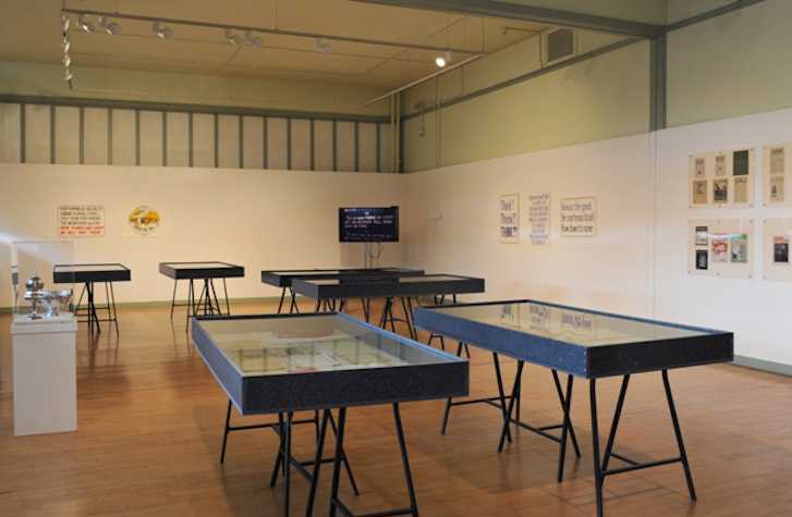 gallery space with work installed on the walls. there are multiple vitrines in the centre of the room.
