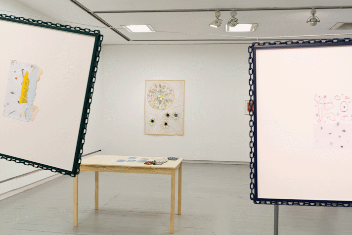 paintings hang on the walls of a gallery. in the middle of the space a wire hangs between two washing line poles, two artworks and a small tv monitor hang from the wire
