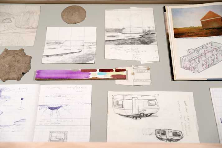 Open books and pencil drawings sit in a glass vitrine