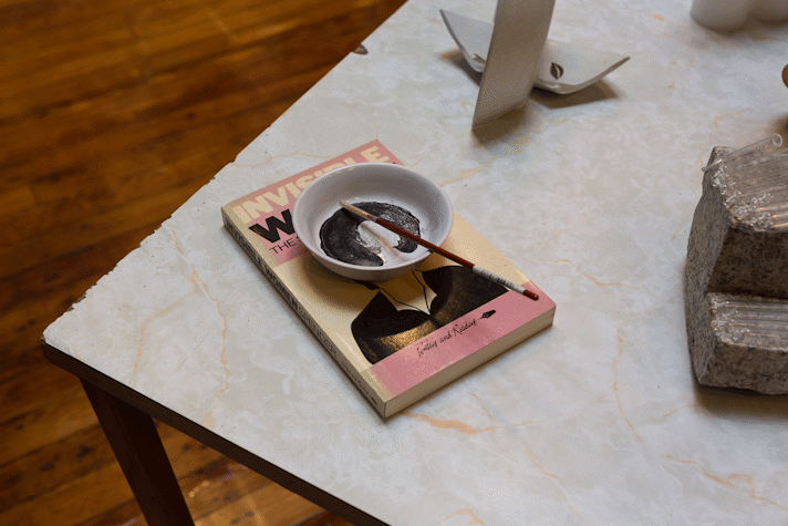 paintbrush and small dish sit on a book called 'Invisible Women'