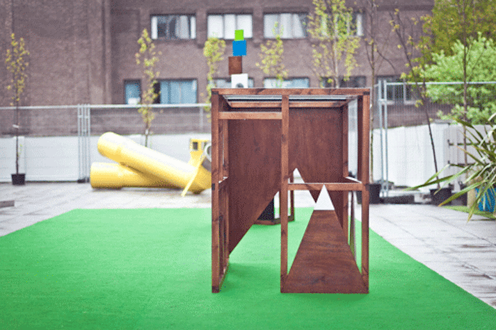 wooden geometric structure on a green rug in an outdoor space