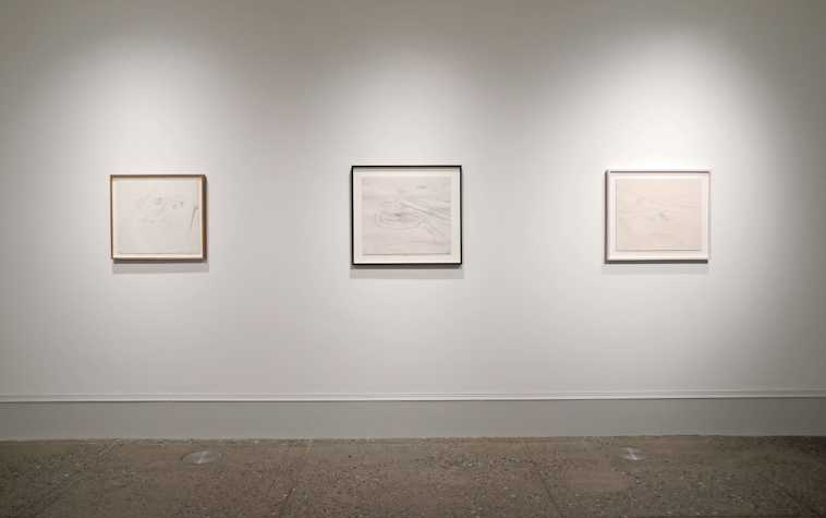 three pencil drawings sit at a distance on a white gallery wall