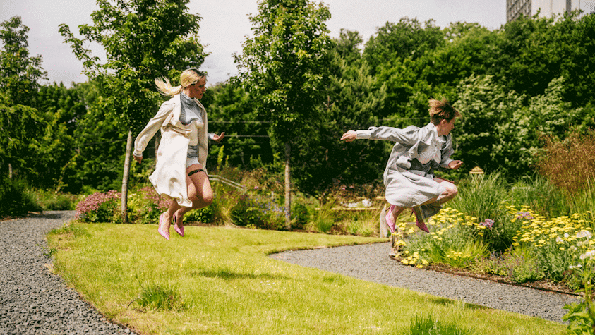 Performers in a garden location. Audience visible in background