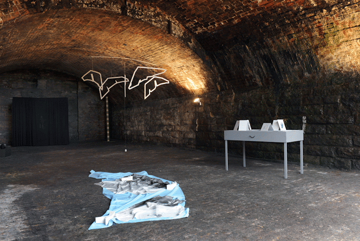 Vaulted basement with suspended neon sculpture in background, as well as other sculptural works