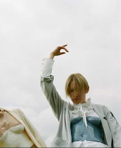A blurred image of a person with blonde hair, liftining their right hand above their head. Their face is obscured.