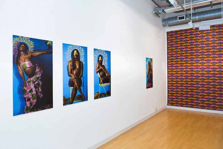 A series of portrait photographs of people of colour on bright blue backgrounds with abstract shapes around their heads, hang on a gallery wall