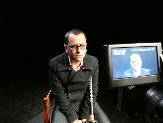 person sat in front of a microphone and video camera. you can see the screen of the video camera.