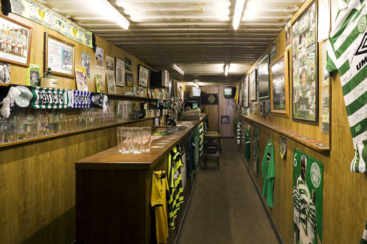 interior of a narrow Glasgow Celtic themed pub with shirts and memorabilia pinned to wood panelled walls