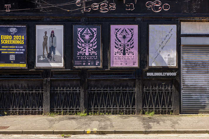 A row of posters are displayed outside on a dark building wall.