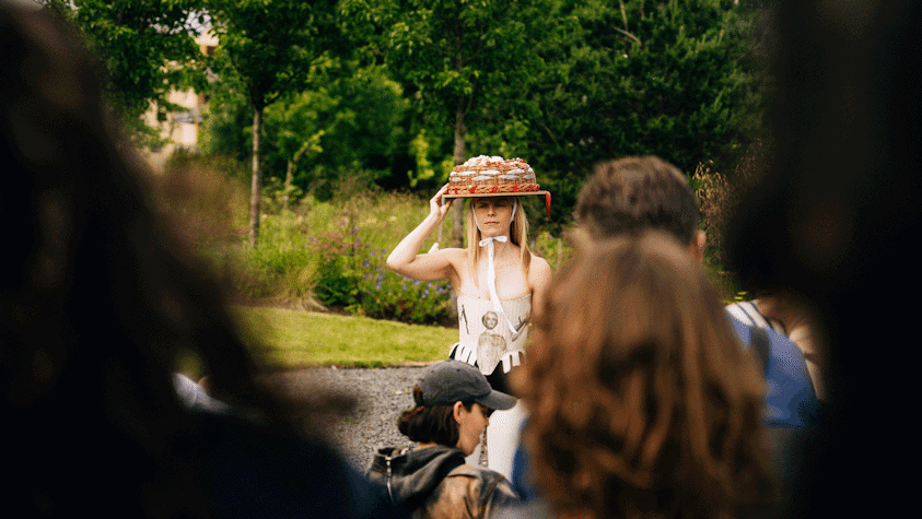 Performer with large hat viewed through gap in audience