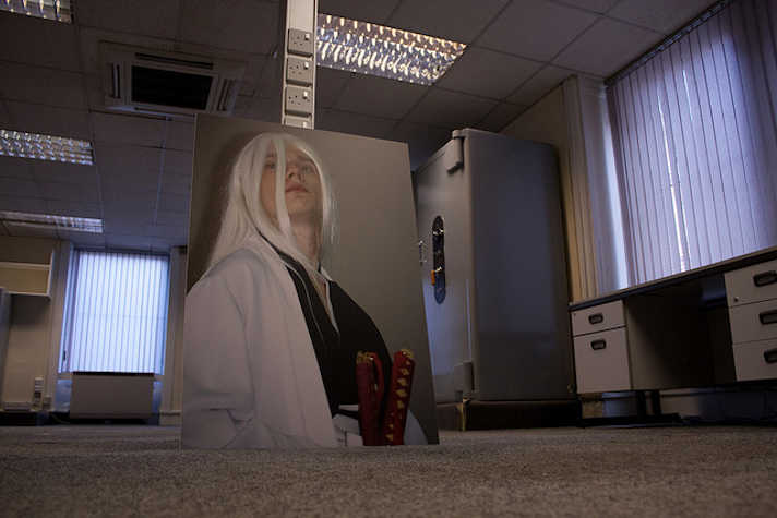 large photographic portrait of a person wearing a long white wig, the image is leaning against a partition wall in an office-like space