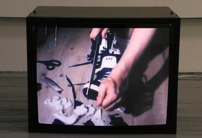 tv monitor on the floor showing someone cut up a pair of nike shoes with a knife