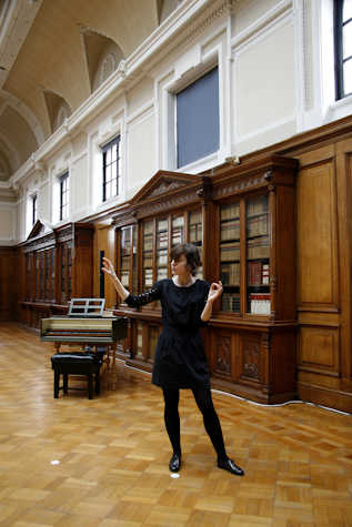 person stood wearing black with arms slightly outstretched in a room in the Mitchell library