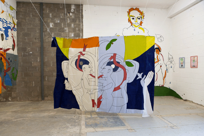 Playful and surreal line drawings of figures with blocks of colour cover a wall and a fabric hanging in an industrial space