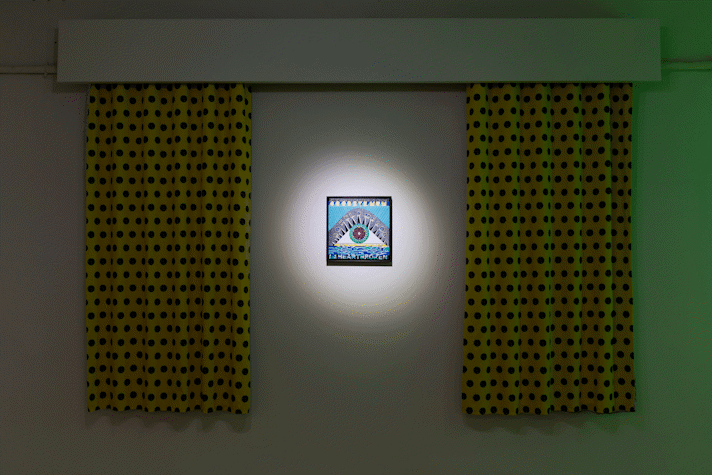 a small painting is hung on the wall and spot-lit, on it are abstract shapes and the words 'my heart is broken', a large curtain hangs either side with a repeat pattern of polka dots