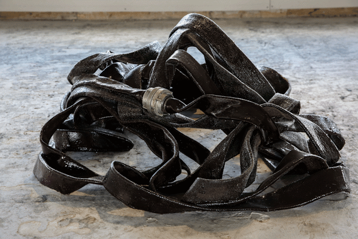 A sculpture of a fire hydrant hose in black on top of the concrete grey floor.