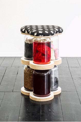 The image shows a sculpture of 6 large glass jars stacked and filled with materials