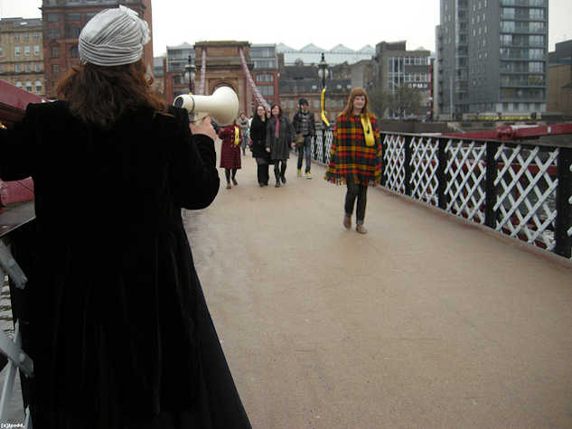 people walking on a bridge. the person in front speaks into a megaphone