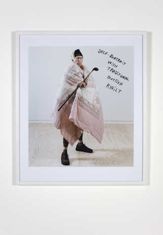 framed image of a person wrapped in a quilt. hand written text on the glass reads 'self-portrait with tradition Scottish kwilt.'