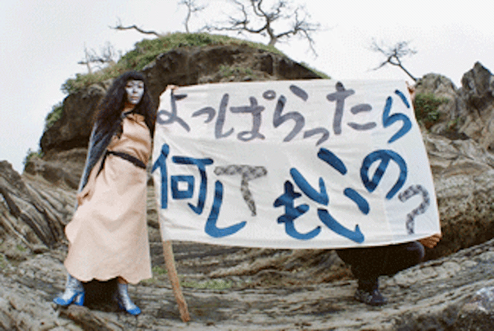 film still - an individual painted in blue holding a banner in front of a landscape