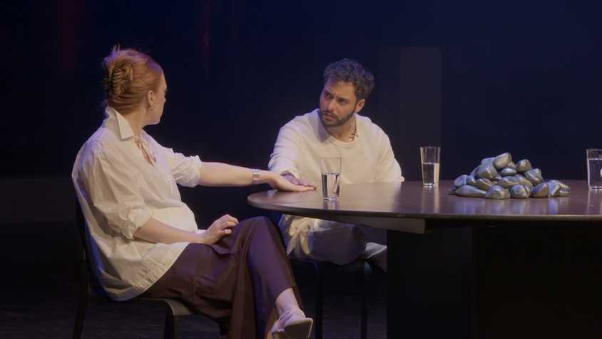 two people sat talking to each other at a round table. there are three glasses of water on the table