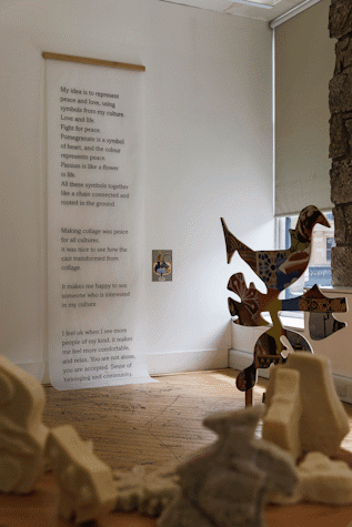 Artwork featuring black and white type is displayed on a wall with blurred sculptures seen in the foreground.