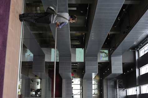 person stood leaning on a bannister in a modern atrium. on each level of the building there is work being projected.