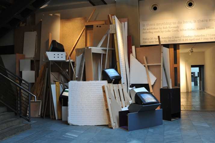 room with wood and crates piled against the wall with two old box televisions resting on top.