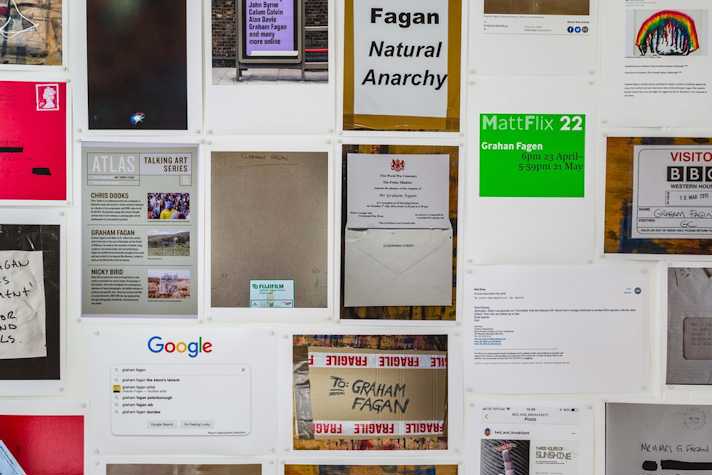 colourful photocopied sheets are pasted to the walls of a small gallery space. The sheets show letters, emails documents and other text-based media.