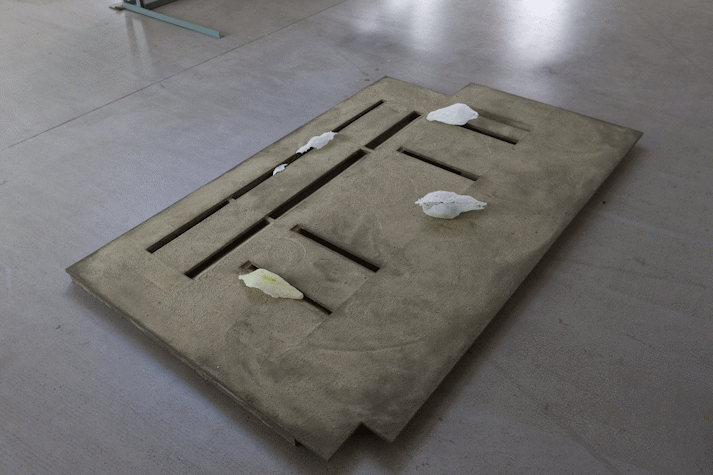 abstract concrete sculpture sits on the floor of a gallery
