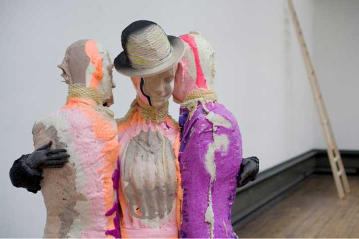 three colourfully painted plaster statues of torsos in embrace