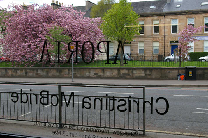 image shot through glass window out onto street. on the window reads the text 'Aporia Christina McBride' but in reverse