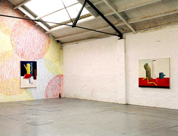 installation view of an exhibition in a large space. one wall is covered in coloured textured circles. two paintings hang, both colourful almost cubist still lifes.