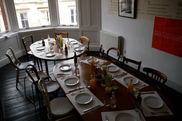 two adjoined dining tables that have been set with placemats, plates and cutlery